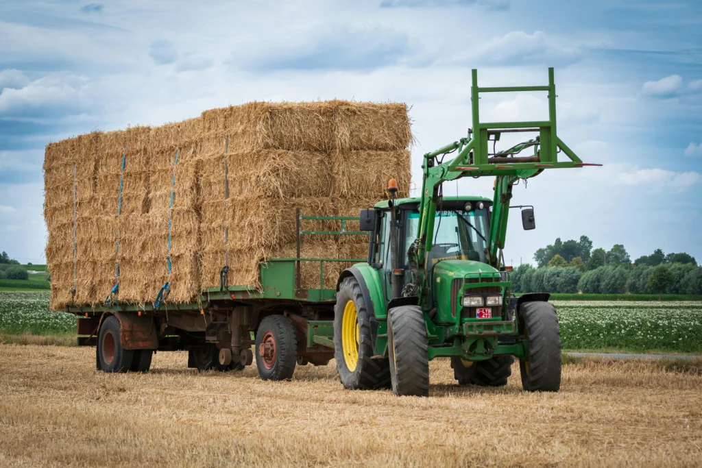 Photo d'un tracteur dans un champ équipé d'un plateau agricole rempli de balles de foin, démontrant l'importance, le gain de temps, et la capacité de charge d'un plateau fourrager pour récolter les balles de foins.