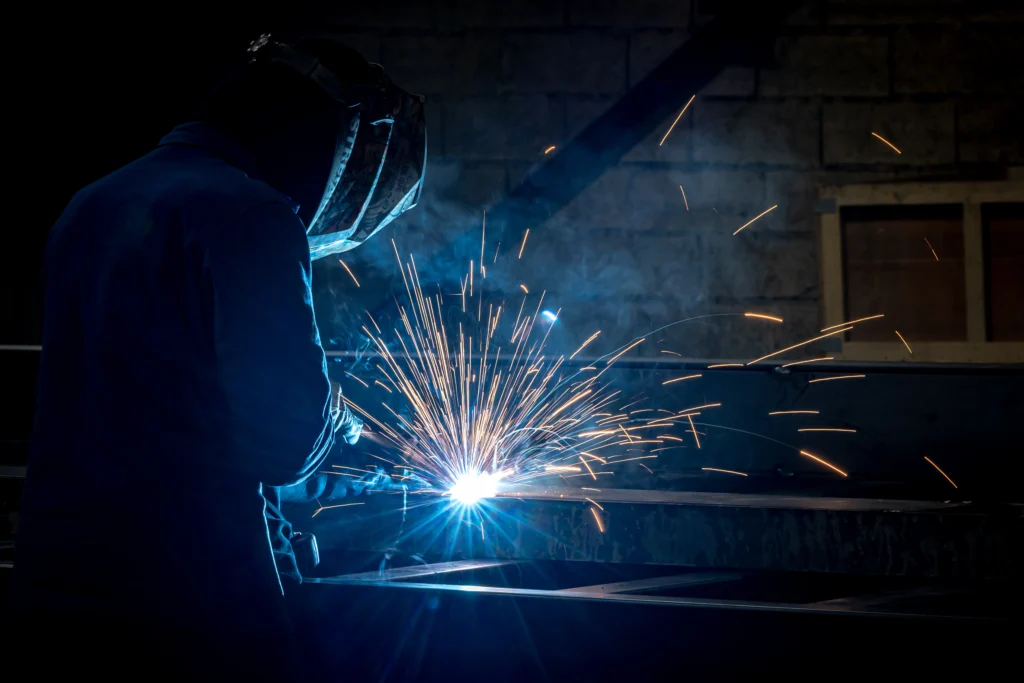 photo d'un soudeur en train de souder une berce en acier dans la société de fabrication française de bennes ampliroll, plateaux agricoles et berces de centrage en acier.
